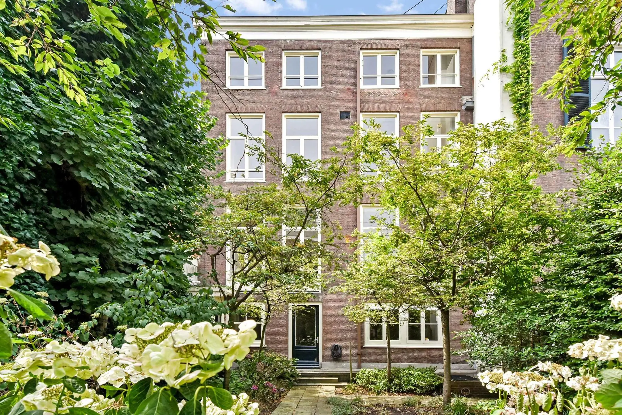 Achtergevel van een klassiek herenhuis aan het Lange Voorhout, omringd door een groene tuin met bloeiende hortensia’s.